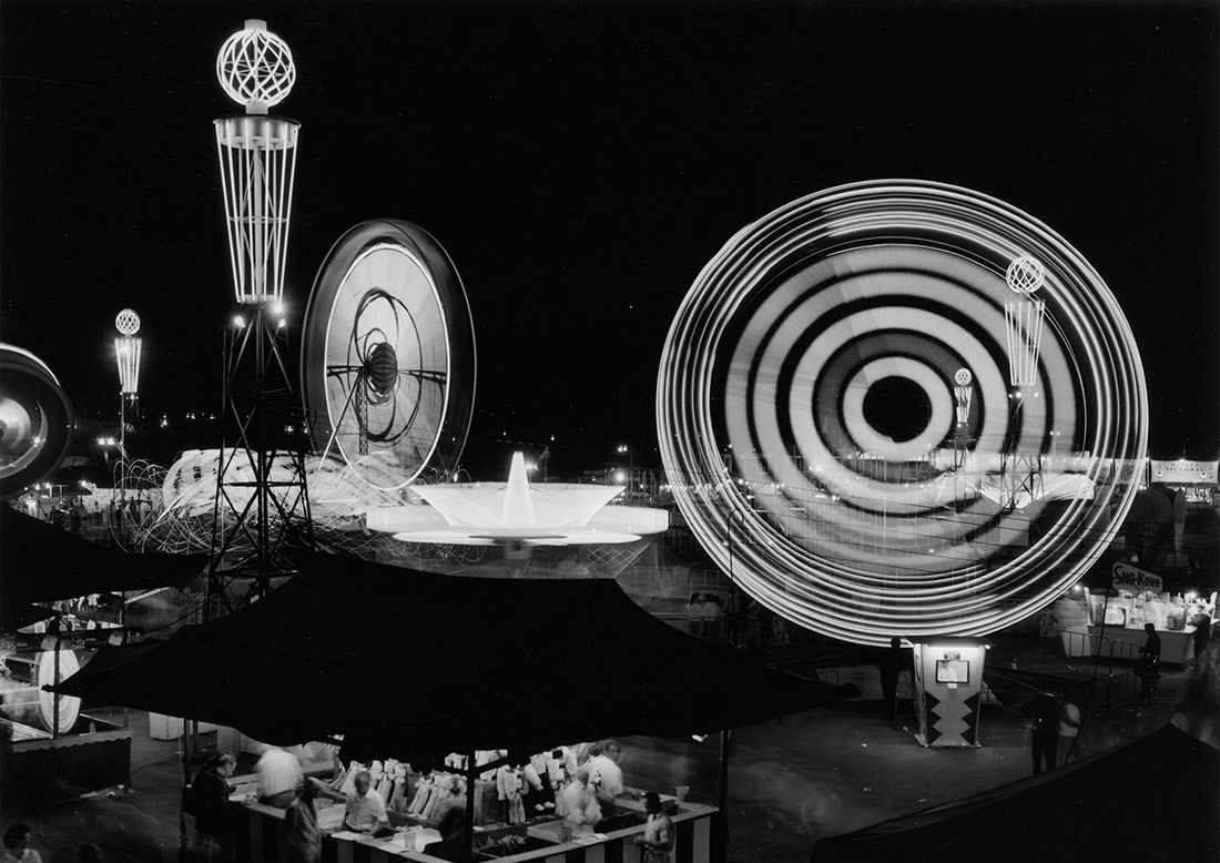 Atracciones iluminadas de noche en el parque Playland. Vancouver, 1961
