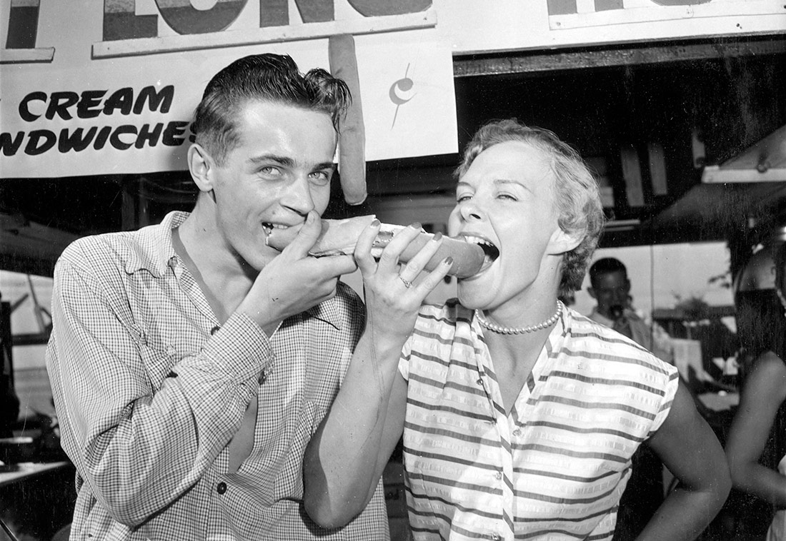 Un hombre y una mujer comiendo perritos calientes de un pie de largo, 1953