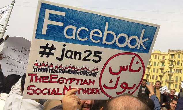 Aman during the 2011 Egyptian protests carrying a card saying "Facebook, #jan25, The Egyptian Social Network".