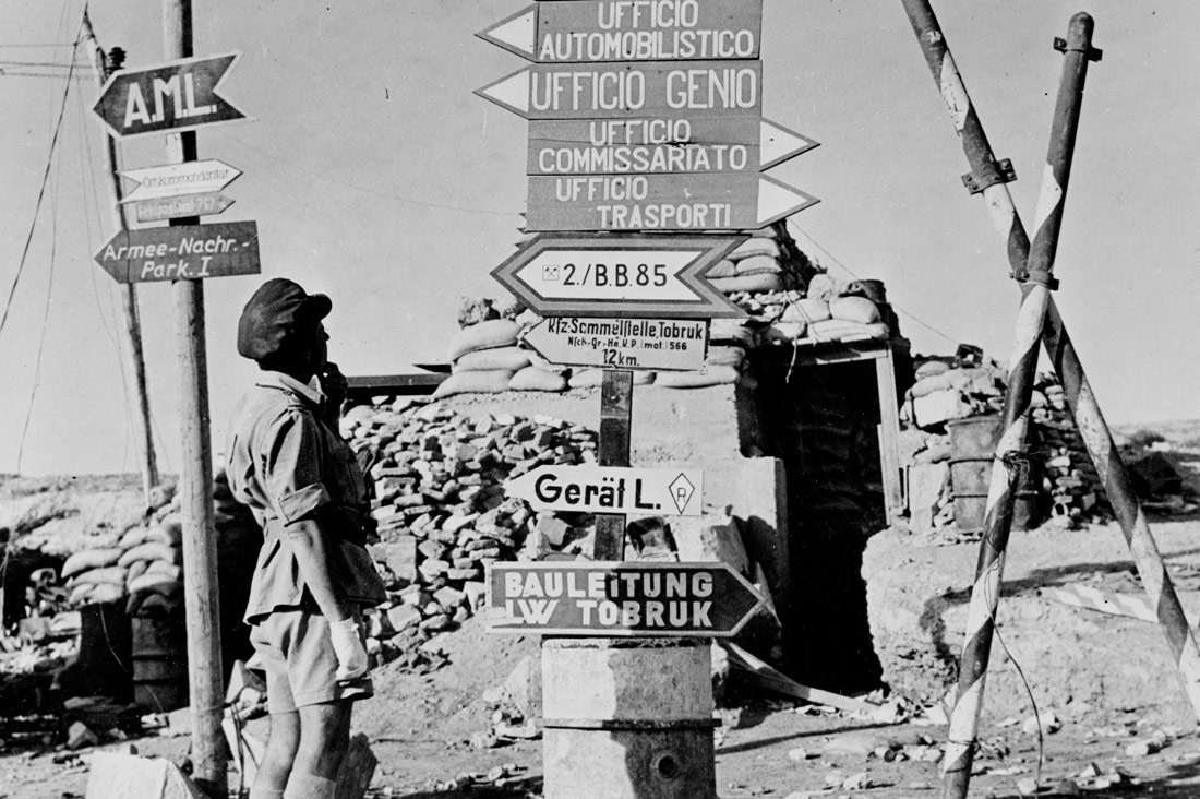 Signposts printed in German and Italian point to former Axis offices at a street corner. Tobruk, Libya, 1942