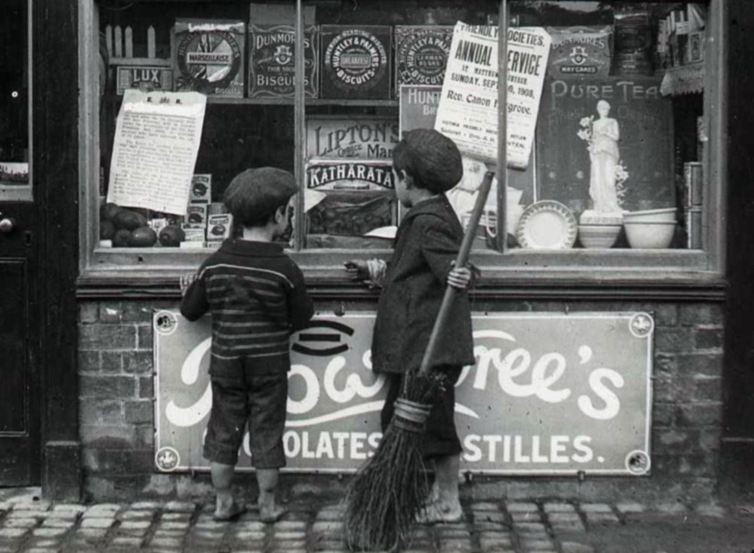 Two children looking at a window of a chocolate shop.