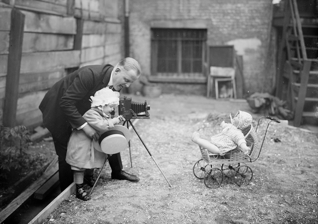 Un hombre con una niña, fotografiando una muñeca en un cochecito de bebé, 1915-120