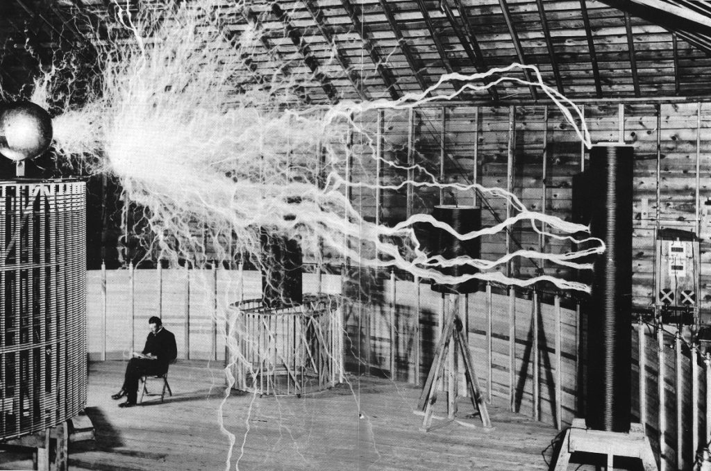 Nikola Tesla sentado en su laboratorio de Colorado Springs con su "transmisor amplificador" generando millones de voltios, 1899
