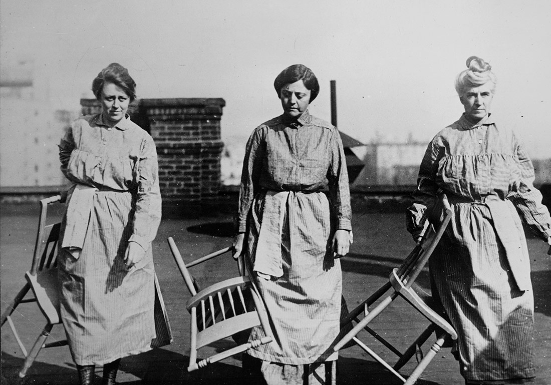 Tres miembros del National Woman's Party en traje de prisión que llevan sillas de madera. Nueva York, 1919